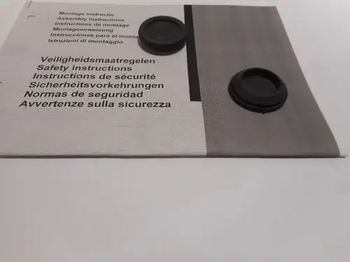 Zwei schwarze Kunststofftulen liegen auf einem Handbuch für Montage- und Sicherheitsanweisungen von Remeha. Die Anleitung ist mehrsprachig und enthält Sicherheitsinformationen.